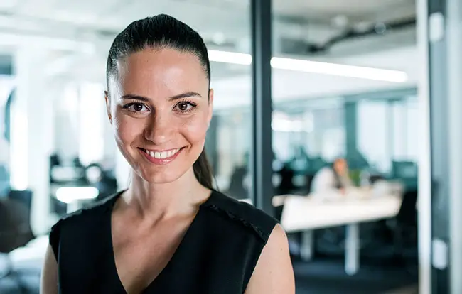 A smiling woman in a black top, in an office setting.