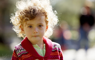 A photograph of a child with curly hair, back-lit by the sun. 